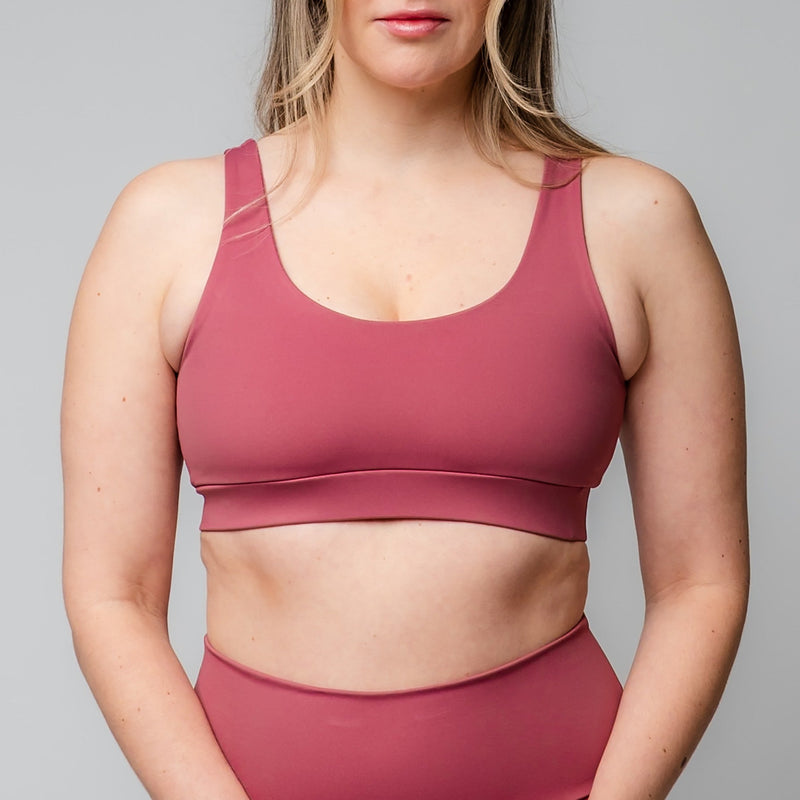 Woman wearing a rose-pink scoop-neck sports bra and matching high-waisted leggings against a grey background.