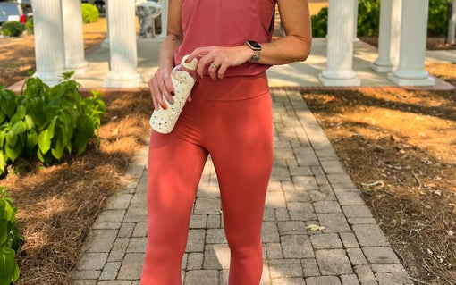 Woman wearing coral high-waisted leggings and a matching athletic top while standing on an outdoor pathway.