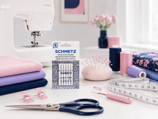 Sewing machine with SCHMETZ knit and stretch needles, folded knits, thread, scissors, pins, and measuring tape.