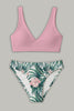 Flat lay of a pink V-neck bikini top and tropical-print bottoms with green leaves and pale pink flowers.