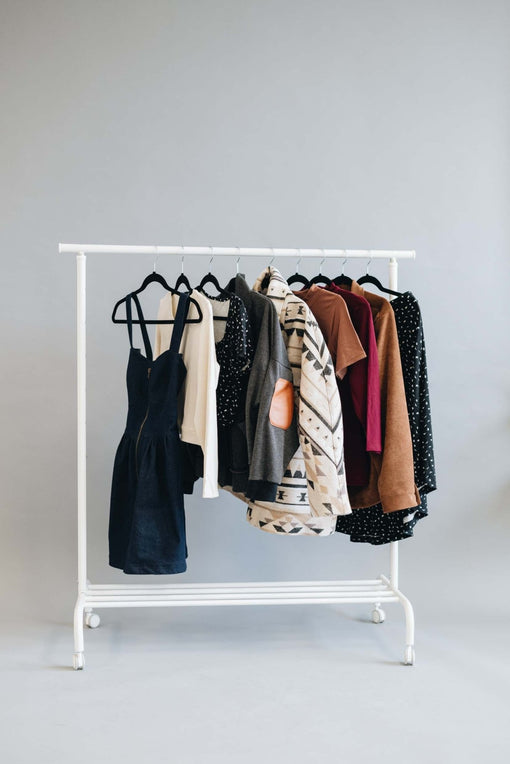 Clothing rack holding dresses, jackets, tops and layers in coordinated neutral and earthy colours.