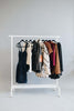 Clothing rack holding dresses, jackets, tops and layers in coordinated neutral and earthy colours.