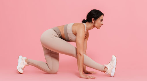 Woman in blush activewear stretching in a low lunge against a pink background