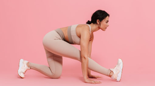 Woman in blush activewear stretching in a low lunge against a pink background