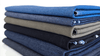 A neatly folded stack of denim and twill fabrics in shades of blue, black, and olive green against a white background.