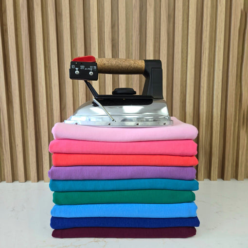 Steam iron resting on a tall stack of folded bamboo french terry fabrics in pink, purple, blue, green and burgundy.