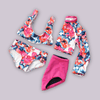 Flat lay of a colorful coordinated swimwear collection, including a bikini, long-sleeve top, shorts, and pink-and-black bottoms.