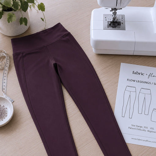 Burgundy handmade leggings beside a sewing machine, measuring tape, pins and Flow Leggings pattern.