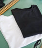 Two folded crew-neck T-shirts in black and white arranged on a green tabletop beside wooden frames