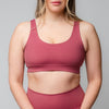 Woman wearing a rose-pink scoop-neck sports bra and matching high-waisted leggings against a grey background.