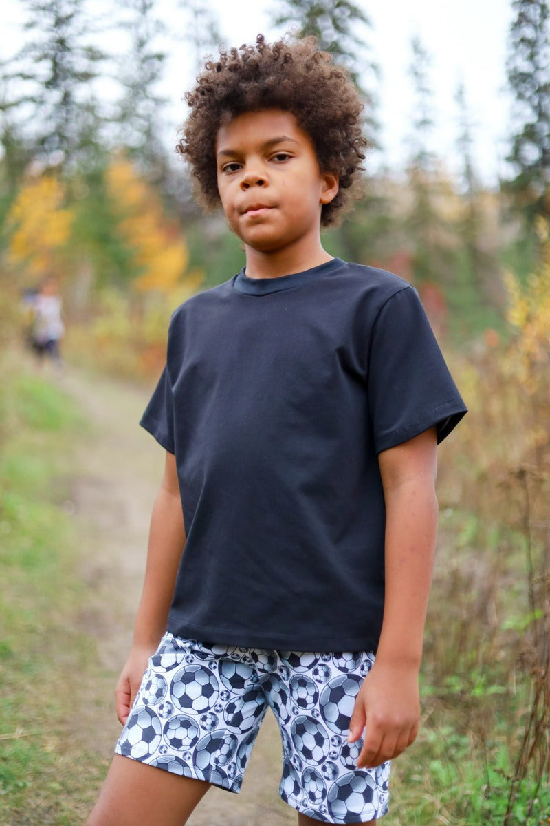 Child wearing a navy cotton jersey T-shirt and patterned shorts outdoors.