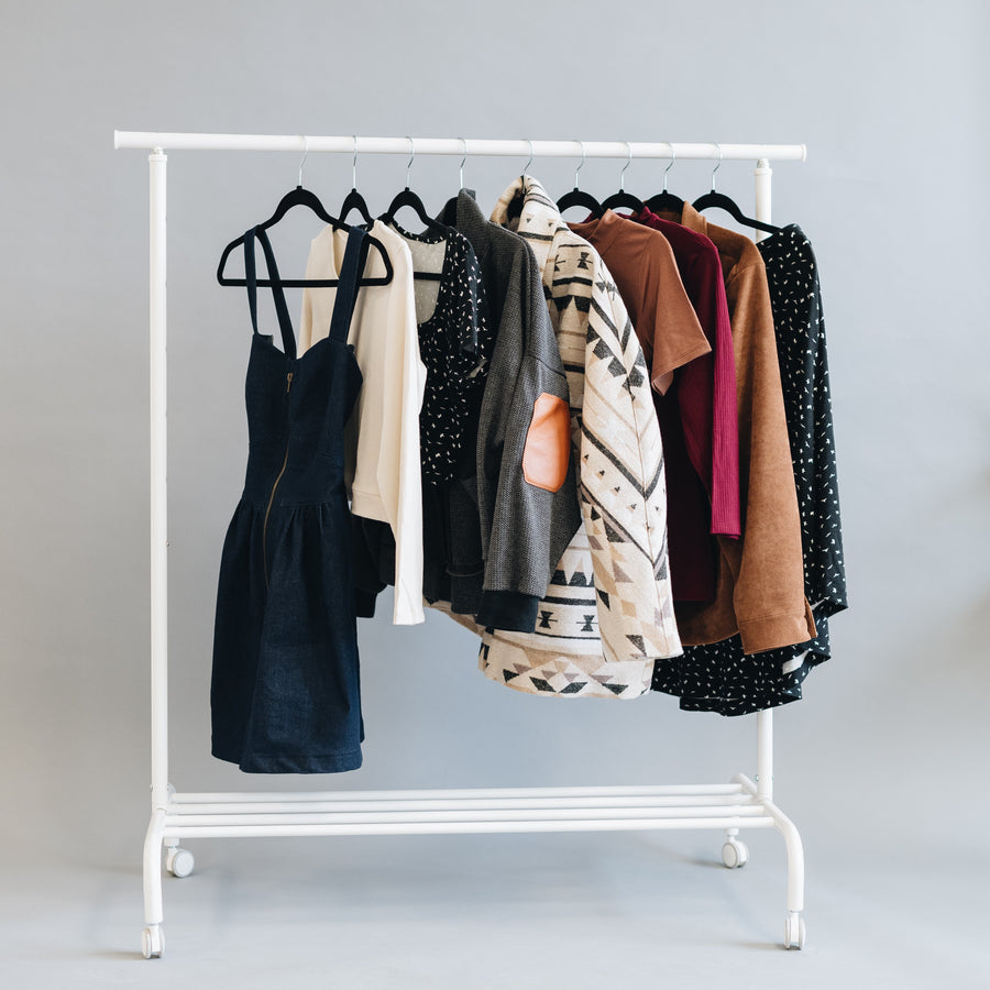 White clothing rack with various garments on a plain background