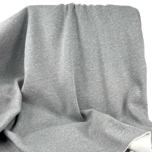 A close-up of draped heather gray fabric with soft folds and a visible white inner lining or backing at the bottom right.