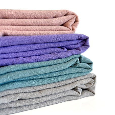 stack of folded linen fabrics in pastel muted colours like peach, purple lilac, robin egg blue and grey steel