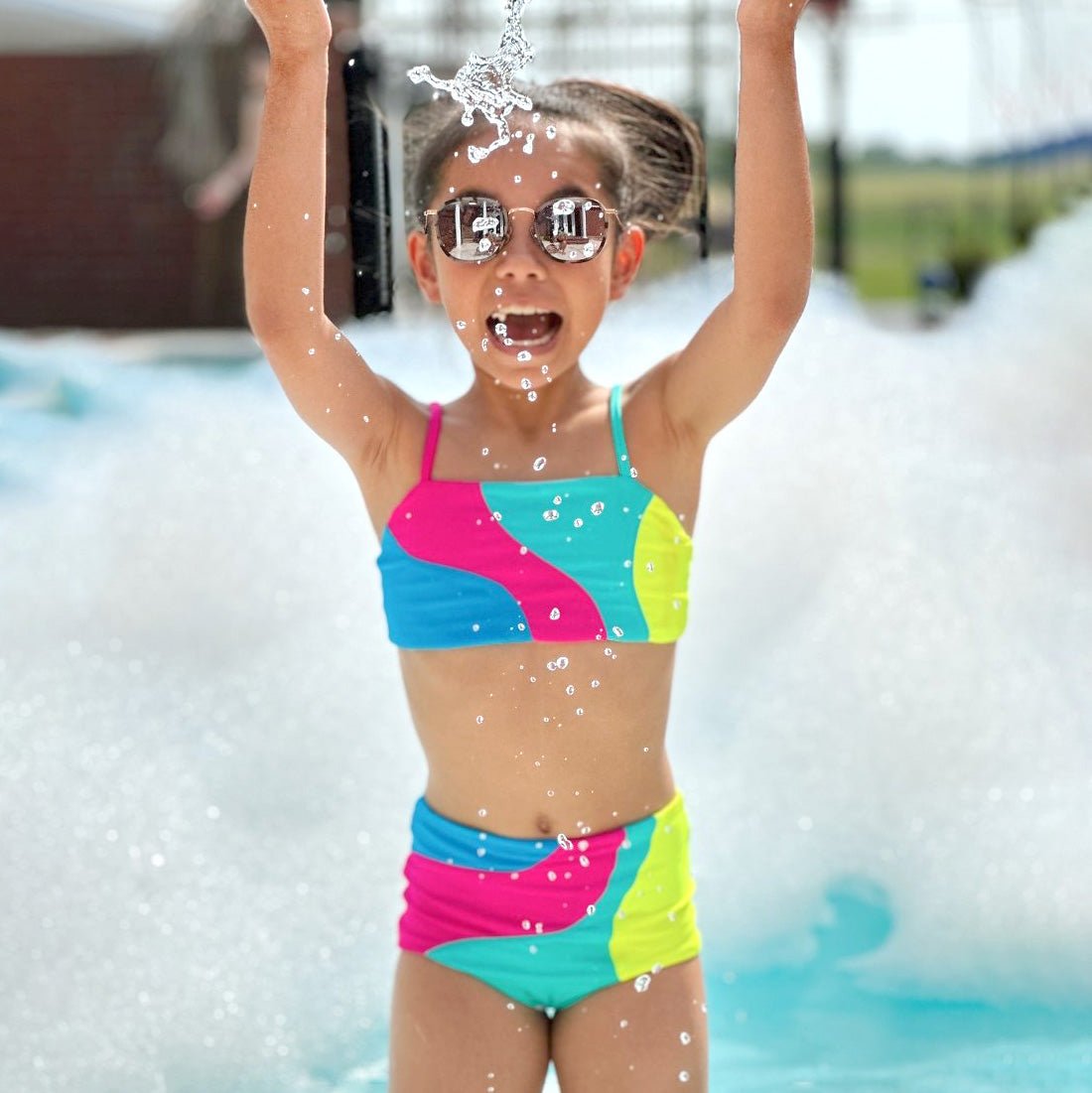 Child in a colorful swimsuit playing in water with water splashes around.