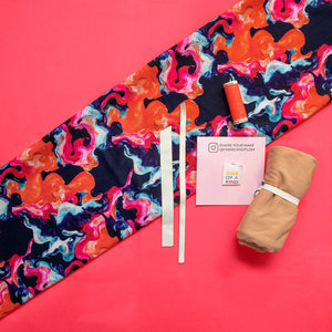 Colorful fabric with a pattern, spools of thread, and a folded brown garment on a pink background.